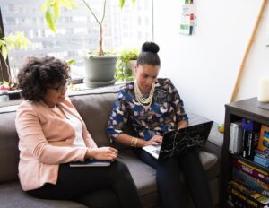 Two women sitting on a couch assess their current pricing on the computer.